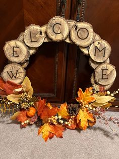 a wreath made out of logs with the word welcome written on it and autumn leaves