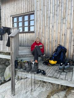 a woman sitting on a porch reading a book next to hiking gear and backpacks