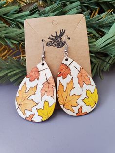 a pair of wooden earrings with leaves painted on them, sitting next to a christmas tree