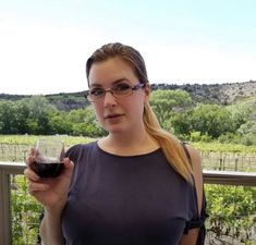 a woman holding a glass of wine in her right hand and looking at the camera