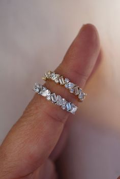 a person's hand holding two rings with diamonds on them and one is wearing a ring