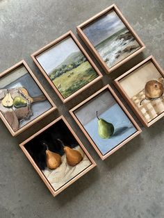 four paintings are displayed in wooden frames on the floor, each with different pears