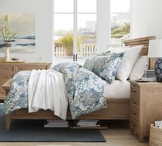 a bedroom with blue and white bedding, wicker furniture and paintings on the wall