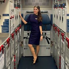 a woman standing in the aisle of an airplane with many lockers on both sides