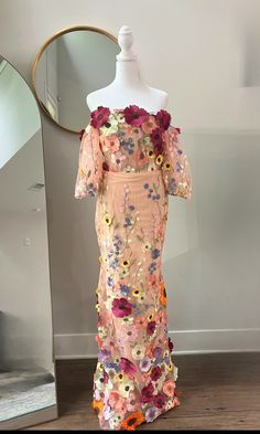 an off the shoulder dress with flowers on it and a mannequin behind it