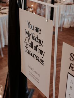 a sign hanging from the side of a pole in front of tables with white linens