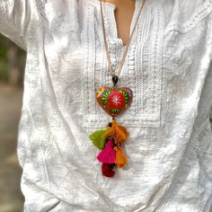 a woman wearing a white shirt and colorful tassels is holding a heart shaped necklace