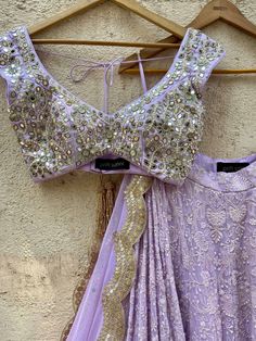 A three-piece lavender lucknowi mirror lehenga set from the Priti Sahni collection. This elegant lavender georgette lehenga with heavy gota, sequins, pearl and zari work border is paired with lavender blouse in raw silk fabric with mirror, pearl and zardozi hand work embroidery. The lehenga has side hanging ball tassels to the waistline. And the blouse has a sequins tassel tie-up at the back. The outfit is completed with a lavender mirror net dupatta with scalloped edging. Lavender Zari Work Sets For Wedding, Lavender Zari Work Wedding Sets, Lavender Wedding Sets With Zari Work, Lavender Wedding Set With Zari Work, Lavender Lehenga With Zari Work For Wedding, Lavender Sharara With Intricate Embroidery For Wedding, Lavender Anarkali Sets For Receptions, Lavender Embroidered Sharara For Wedding, Lavender Wedding Choli With Resham Embroidery