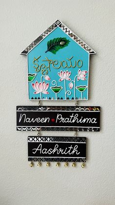 three signs are hanging on the wall in front of a white wall with flowers and a house