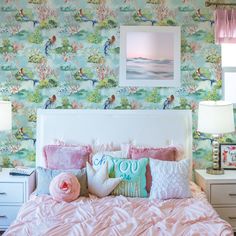 a bed with pink sheets and pillows in front of a wallpapered bedroom area