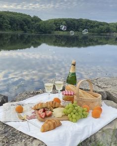 a picnic with bread, grapes and wine on the rocks near a body of water