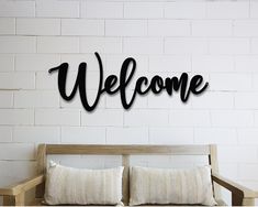 a welcome sign mounted to the side of a white brick wall next to a wooden bench