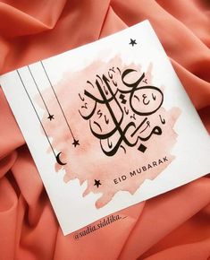 an islamic calligraphy is displayed on a pink fabric with stars and crescents in the background