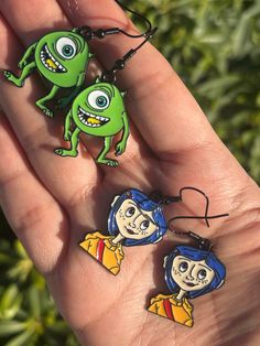 two cartoon keychains in the palm of someone's hand, one with an alien face on it