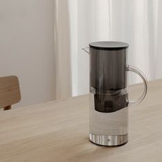 a glass coffee maker sitting on top of a wooden table next to a white curtain