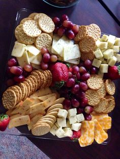 a glass plate filled with crackers, grapes and strawberries on top of a wooden table