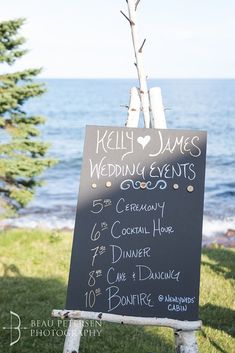 a chalkboard sign with the names of wedding events written on it in front of an ocean view