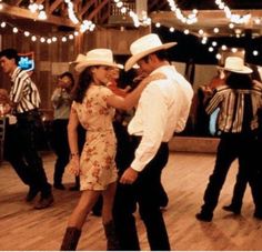 a man and woman dancing on a dance floor with lights strung over the top of them