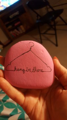 a person holding a pink rock with the word hangin'there written on it