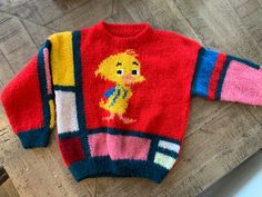 a colorful sweater with an image of a cartoon character on the front and back, sitting on a wooden floor