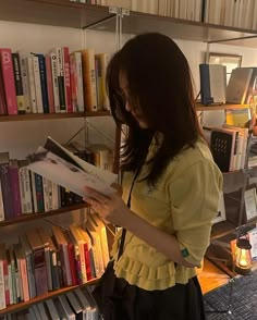 a woman standing in front of a bookshelf holding a book and looking at it