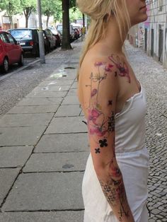 a woman with a flower tattoo on her arm and shoulder is walking down the street