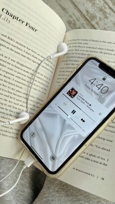 an iphone with headphones is laying on top of an open book and earbuds are plugged into it