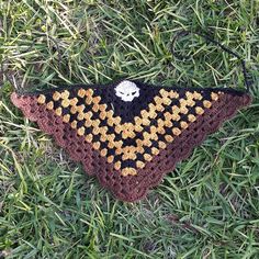 a crocheted triangle on the ground with grass around it and a white skull in the center