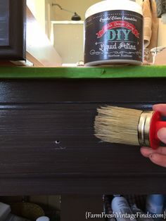 a person is holding a paint brush and painting the side of a dresser with dark wood