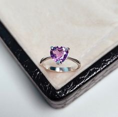 a pink heart shaped ring sitting on top of a white table next to a black box