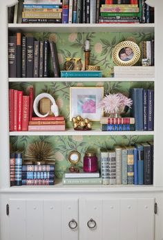 the bookshelf has many different types of books on it and is decorated with green wallpaper