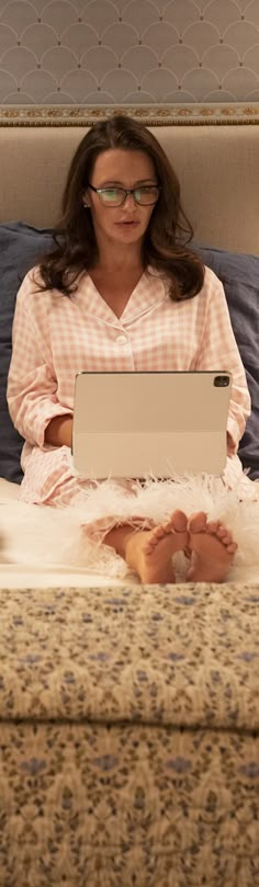 a woman is sitting on her bed with a laptop computer in front of her face