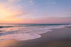 the sun is setting over the ocean with waves coming in to shore and sand on the beach