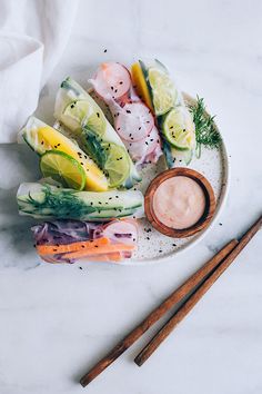 an assortment of vegetables on a plate with chopsticks and dipping sauce next to them