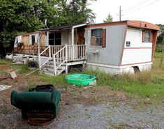 a mobile home sits in the grass next to a green trash can and garbage can