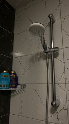 a shower head with water running from it and soap on the shelf next to it