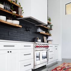 a kitchen with white cabinets and black tile backsplash, stainless steel range hood