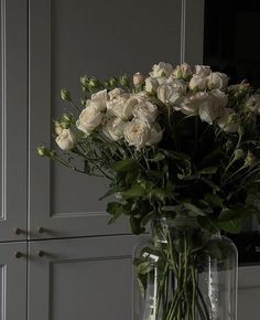 a vase filled with white flowers sitting on top of a table next to a wall