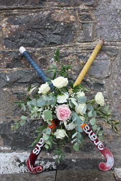 a bouquet of flowers with two baseball bats on the side of a stone wall behind it