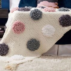 a crocheted blanket with pom - poms on it sitting on a bed