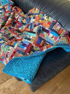 a couch with a quilt on top of it next to a black leather chair and wooden floor