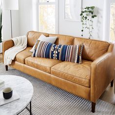 a tan leather couch in a living room with pillows on the armrests and coffee table