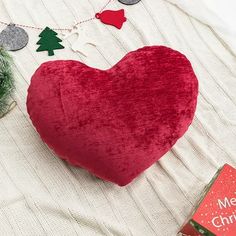 a red heart shaped pillow sitting on top of a bed next to a christmas tree