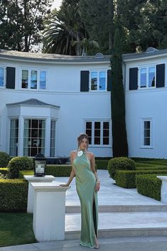 a woman standing in front of a large white house wearing a green dress and heels