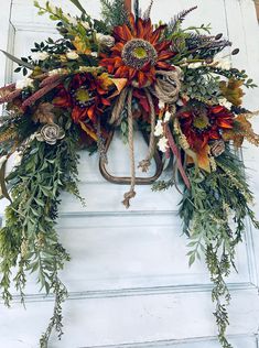 a wreath hanging on the front door of a house with flowers and foliage around it