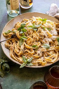 a plate of pasta with basil and parmesan cheese on it next to two glasses