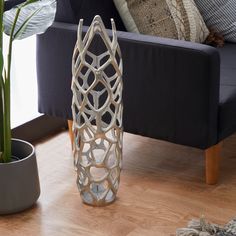 a white vase sitting on top of a wooden floor next to a blue couch and potted plant