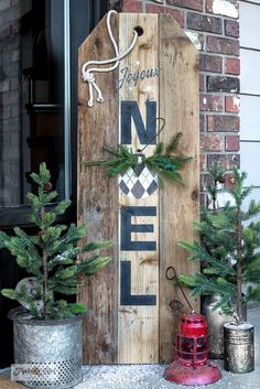 a wooden sign sitting on the side of a building next to christmas trees and potted plants