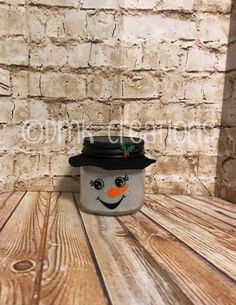 a ceramic snowman pot sitting on top of a wooden table next to a brick wall