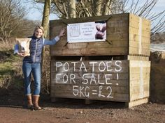 a woman standing next to a wooden box with potatoes for sale written on the side